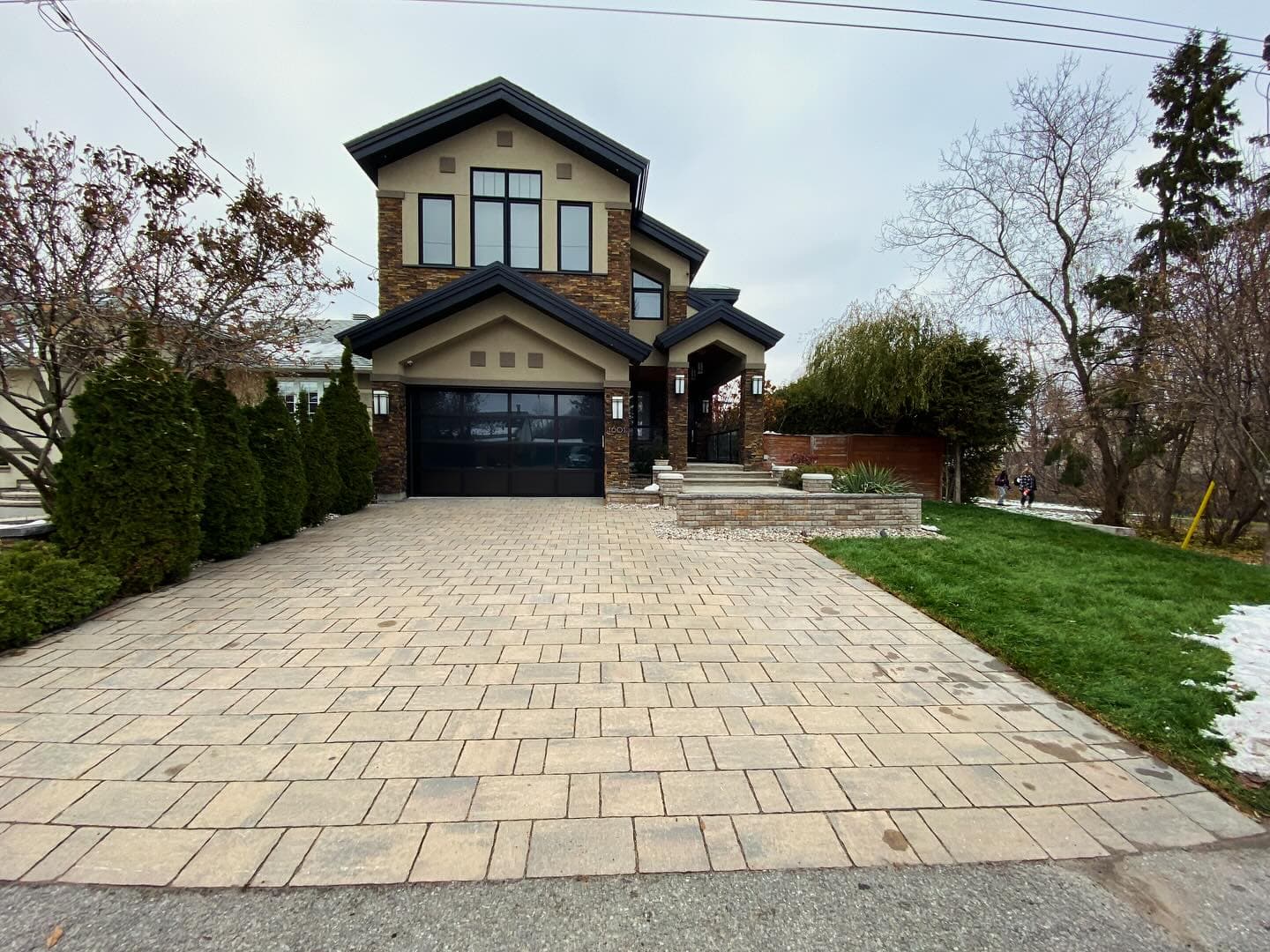 Modern two-story home with stone accents and a wide brick-paved driveway under cloudy skies.