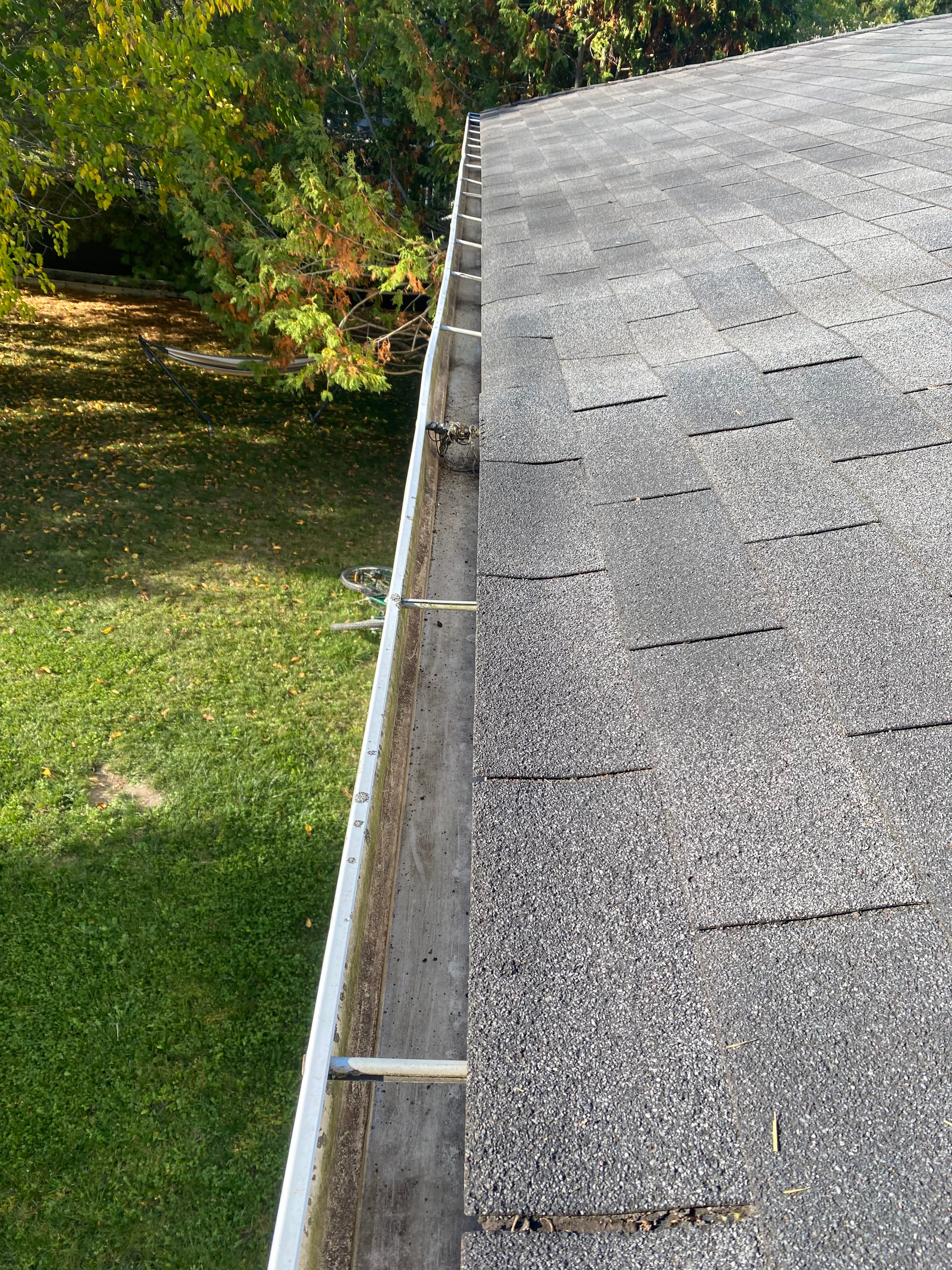 Grey shingled roof and white gutter overlooking a green lawn with trees and a bicycle.